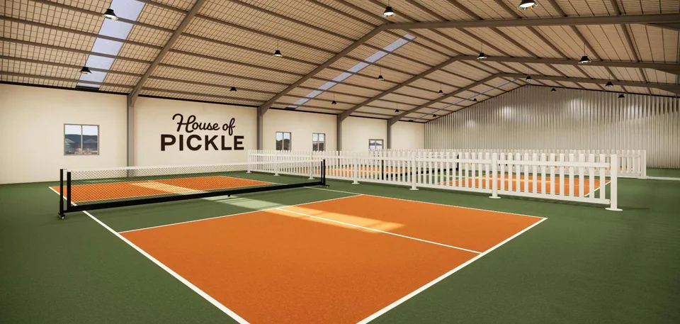 An indoor pickleball court with white picket barriers and the House of Pickle name on the wall